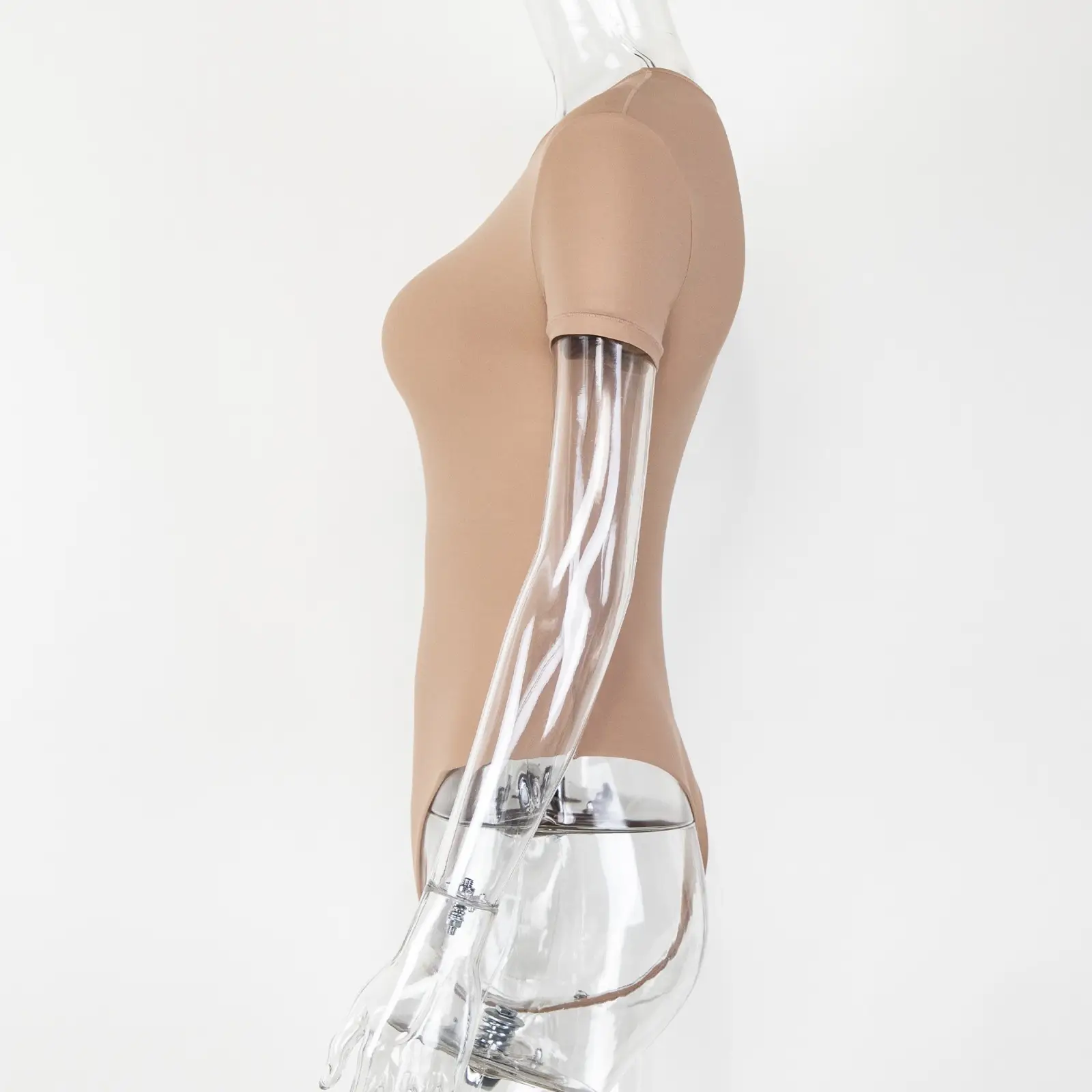 Transparent acrylic mannequin wearing a beige t-shirt bodysuit from the side over a white wall.