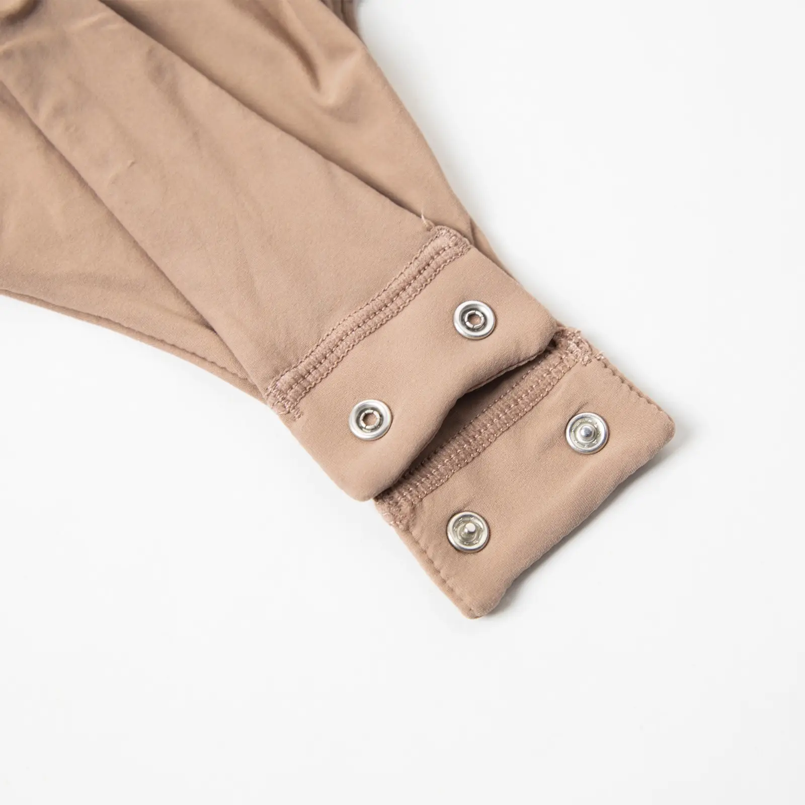 The bottom thong snap closure design of a beige bodysuit.